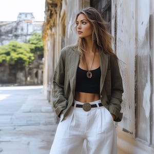 Peut inclure: Une femme portant une veste en lin vert sur un haut court noir et un pantalon en lin blanc. Elle porte un collier en or avec un pendentif circulaire et une ceinture tissée noire avec une grande boucle dorée.