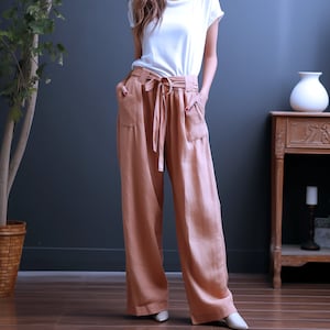 May include: A woman wearing a white t-shirt and wide-legged, light brown trousers with a matching fabric belt.