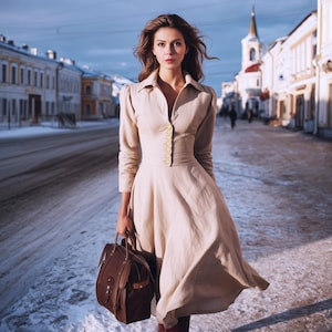 Puede incluir: Una mujer con un vestido beige con botones dorados y un bolso de cuero marrón camina por una calle cubierta de nieve. El vestido tiene mangas largas y una falda acampanada. El bolso es rectangular con un asa superior.