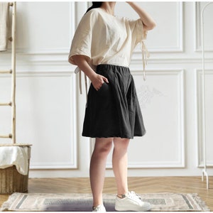 Op de afbeelding: Een vrouw draagt een wit linnen topje en een zwarte linnen broek. De broek heeft een wijde pijp en een ontspannen pasvorm.