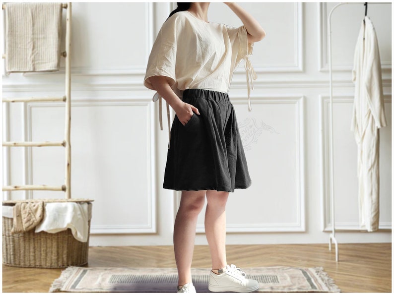 Op de afbeelding: Een vrouw draagt een wit linnen topje en een zwarte linnen broek. De broek heeft een wijde pijp en een ontspannen pasvorm.