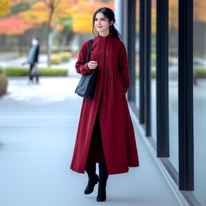 May include: A woman wearing a long, burgundy dress with a button-up front and a black tote bag. She is walking on a pavement in front of a building with large windows.