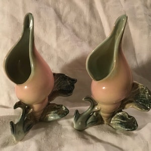 May include: Two pink and green ceramic vases shaped like seashells with a fish tail base.