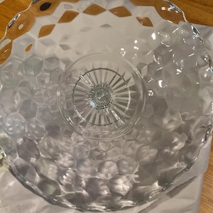 May include: A clear glass cake stand with a scalloped edge and a textured, diamond-shaped pattern. The stand has a center pedestal with a starburst design.