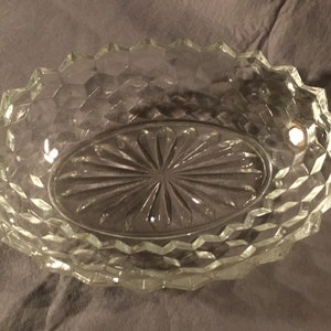 May include: A clear glass oval serving dish with a diamond pattern around the edge and a starburst pattern in the center.