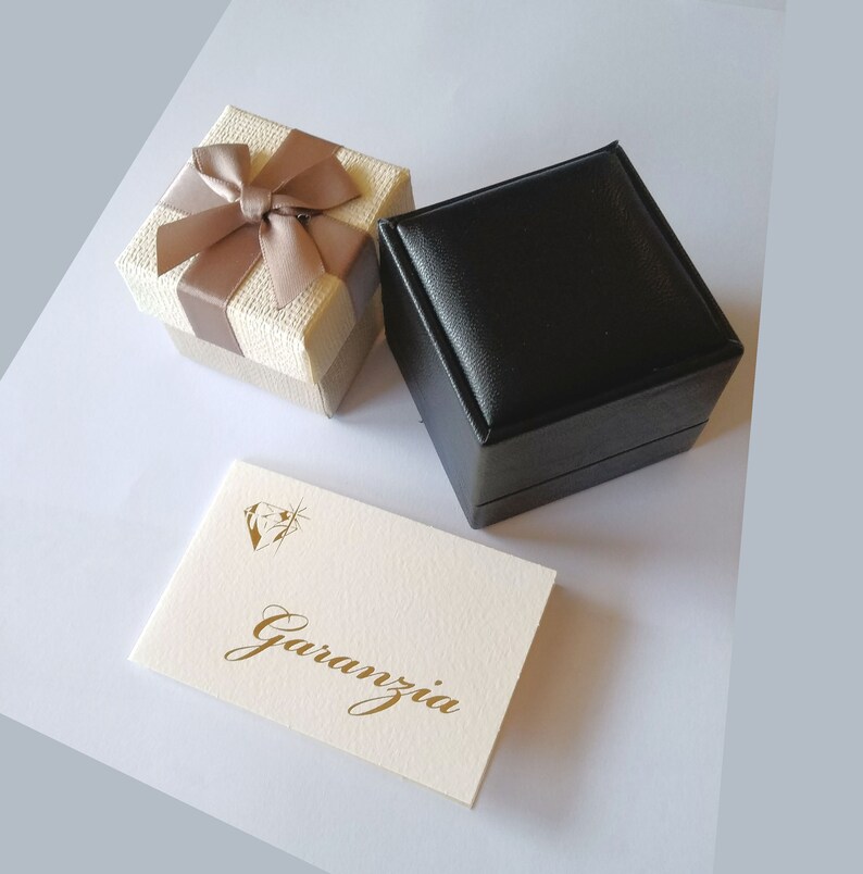 May include: Two gift boxes, one beige with a brown bow and one black, with a white card that says "Garanzia" in gold lettering.