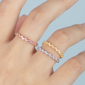May include: Two delicate rings with small, clear stones set in a continuous line. The ring on the top is gold, and the ring on the bottom is silver.