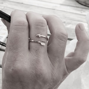 May include: A gold ring with two arrow designs. The ring is worn on a person's finger.