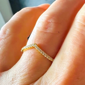 May include: A gold band ring with a V-shaped design set with small clear stones.
