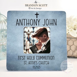 May include: A blue framed photo with the text "ANTHONY JOHN" and "FIRST HOLY COMMUNION ST. ANNE'S CHURCH 05,24,25". The photo features a young boy in a suit praying with a book.