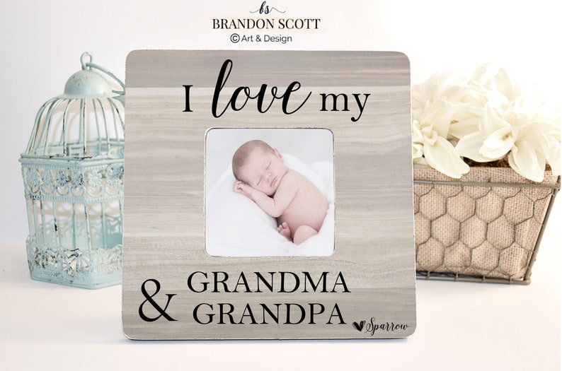 May include: A light gray wooden picture frame with a white mat and a photo of a sleeping baby. The frame has the text "I love my Grandma & Grandpa" with a small heart and the word "Sparrow" below.