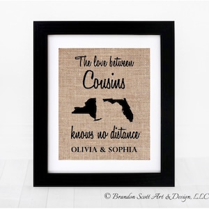 May include: A framed burlap print with the text "The love between Cousins knows no distance Olivia & Sophia". The print features black silhouettes of the states of New York and Florida.
