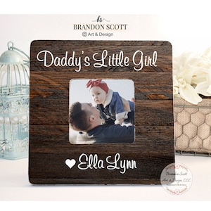 May include: A rustic wooden picture frame with a white inscription that reads "Daddy's Little Girl" and a heart with the name "Ella Lynn". A photo of a father holding his daughter is in the frame.
