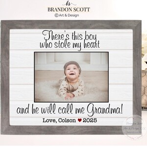 May include: A framed photo with a gray wooden frame. The photo features a baby wearing a hat and smiling. Text on the frame reads "There's this boy who stole my heart and he will call me Grandma!" with "Love, Colson 2025" below.