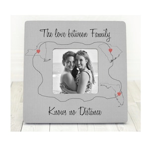 May include: A gray picture frame with a black and white photo of two women hugging. The frame has a design of a map with hearts and the text "The love between family knows no distance".
