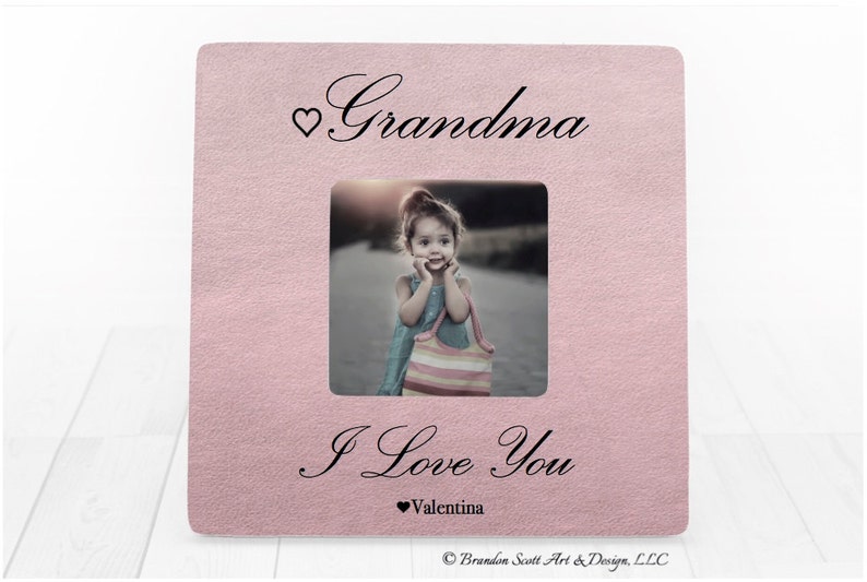 Op de afbeelding: Roze fotolijst met een witte passe-partout en een foto van een jong meisje. De lijst heeft de tekst "Grandma" bovenaan en "I Love You" met een hartje en de naam "Valentina" onderaan.
