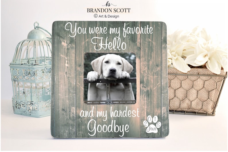 Pu&ograve; includere: Una cornice per foto in legno con una foto di un cane. La cornice ha il testo "You were my favorite Hello and my hardest Goodbye" e le date "2011" e "2018" con un'impronta di zampa e il nome "Java" sotto.