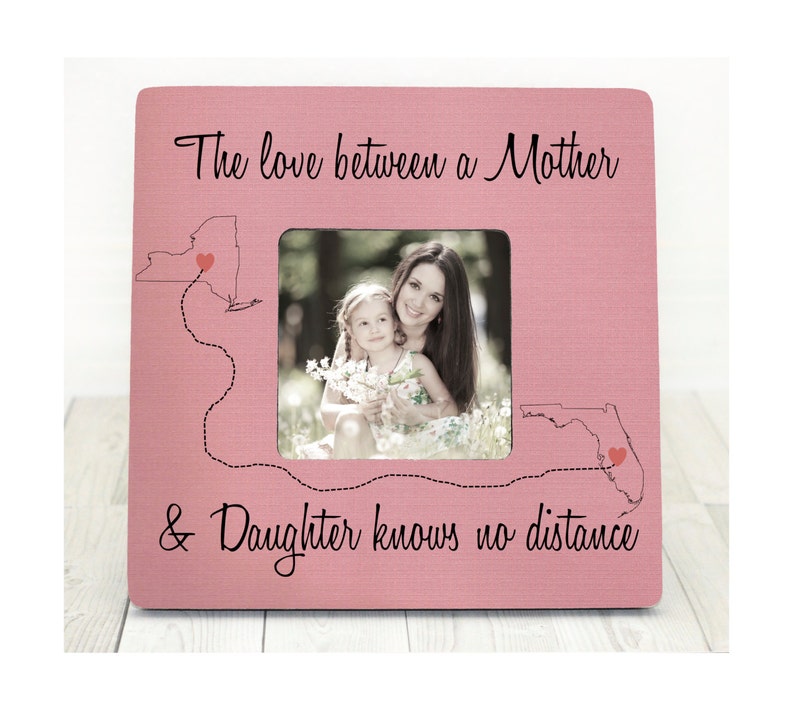 May include: Pink wooden picture frame with a photo of a mother and daughter. The frame has a quote that reads "The love between a Mother & Daughter knows no distance" and outlines of New York and Florida with hearts.