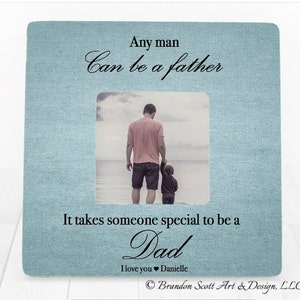 May include: A light blue picture frame with a white linen texture. The frame has a photo of a father and child walking on a beach. The text reads "Any man can be a father. It takes someone special to be a Dad. I love you Danielle. Brandon Scott Art & Design, LLC."