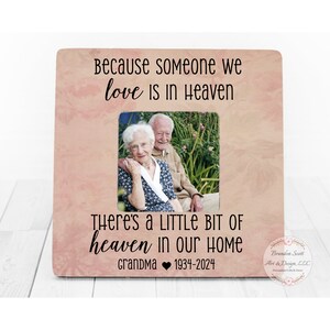 Puede incluir: Un marco de fotos de madera con fondo rosa y una foto de una pareja mayor. El marco tiene el texto "Because someone we love is in Heaven There's a little bit of heaven in our home Grandma 1934-2024".