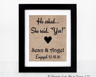 Puede incluir: Una impresión de arpillera con texto negro que dice "He asked... She said, "Yes!" Sean & Angel Engaged 10.18.16" con un corazón negro en el centro.