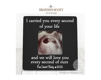 May include: Black wooden picture frame with a white inscription that reads "I carried you every second of your life and we will love you every second of ours Our Sweet Baby 2025". The frame has a clear window for a photo, and a black and white ultrasound image is visible in the window.