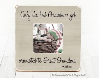 May include: A light brown wooden picture frame with a white border. The frame has a photo of a baby wearing a red and green elf hat in a wicker basket. The text on the frame reads "Only the best Grandmas get promoted to Great Grandma ♥ Ethan".