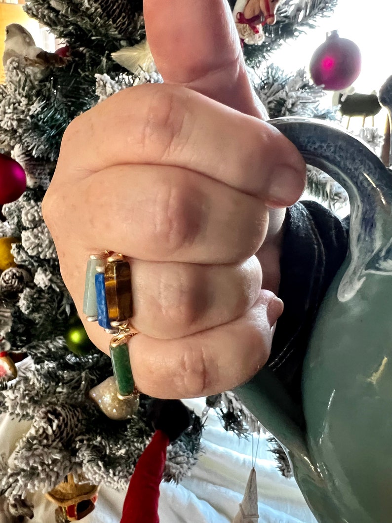 Puede incluir: Tres anillos de oro con piedras preciosas de diferentes colores. Los anillos est&aacute;n apilados en un dedo. Las piedras preciosas son azules, verdes y azul oscuro.