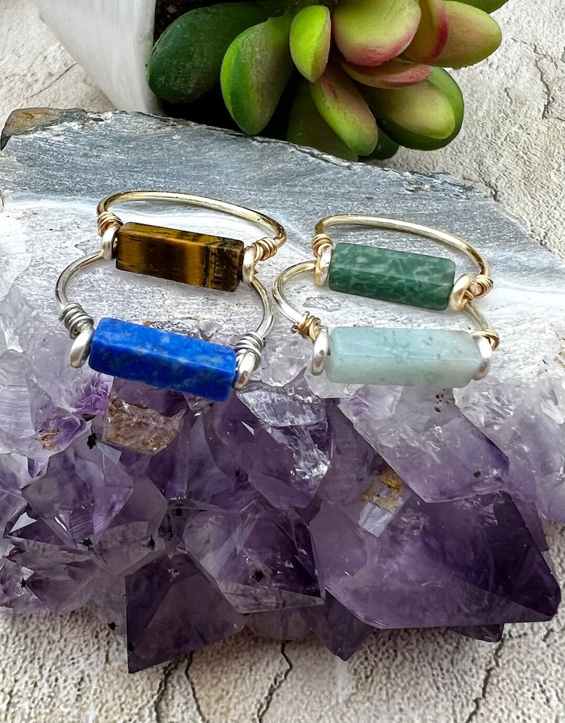 Puede incluir: Cuatro anillos de oro con piedras de diferentes colores. Las piedras son un ojo de tigre, una piedra verde, una piedra azul y una piedra verde claro.