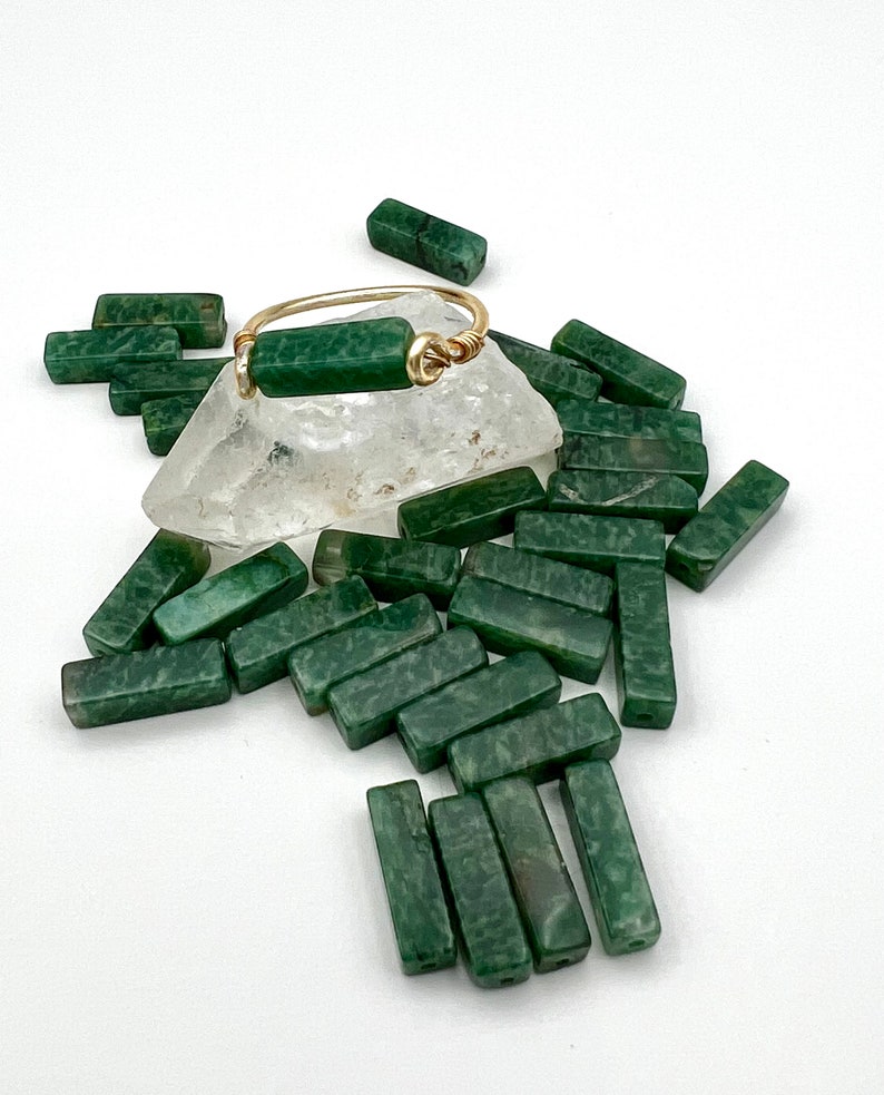 Puede incluir: Un anillo de oro con una barra de piedra verde. El anillo est&aacute; rodeado de muchas barras de piedra verde.