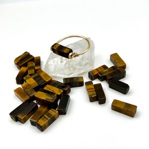 Puede incluir: Un anillo de oro con una piedra rectangular de ojo de tigre. El anillo est&aacute; rodeado de piedras sueltas de ojo de tigre.