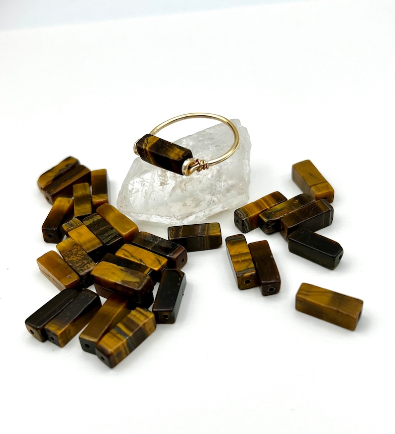 Puede incluir: Un anillo de oro con una piedra rectangular de ojo de tigre. El anillo est&aacute; rodeado de piedras sueltas de ojo de tigre.