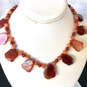May include: A necklace made with carnelian beads and carnelian pendant drops. The necklace is brown, orange, and red.