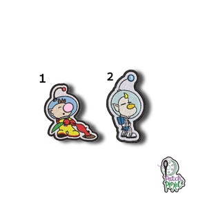 Könnte beinhalten: Zwei gestickte Bügelbilder mit Figuren aus der Videospielserie 'Kirby'. Das erste Bügelbild zeigt eine Figur in einem blau-weißen Raumanzug mit einer rot-gelben Blume. Das zweite Bügelbild zeigt eine Figur in einem blau-weißen Raumanzug mit einem gelben Schnabel.