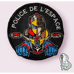 Könnte beinhalten: Ein schwarzer gestickter Aufnäher mit weißem Rand. Der Aufnäher zeigt eine Comicfigur, die ein Motorrad fährt. Der Text "POLICE DE L'ESPACE" ist um den Rand des Aufnähers herum geschrieben.