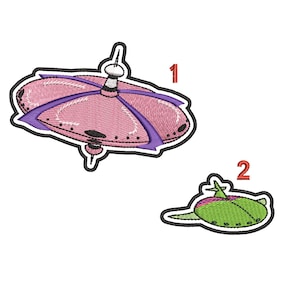 Op de afbeelding: Twee geborduurde patches met ruimteschepen. De eerste patch is roze met paarse accenten en een witte koepel bovenop. De tweede patch is groen met roze accenten. De patches zijn genummerd 1 en 2.