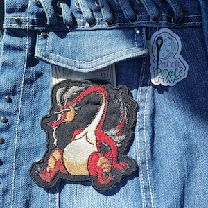 May include: A red and white embroidered dragon patch on a blue denim jacket. The patch is sewn on the pocket of the jacket. The patch has the text "Patch Pixel" on it.