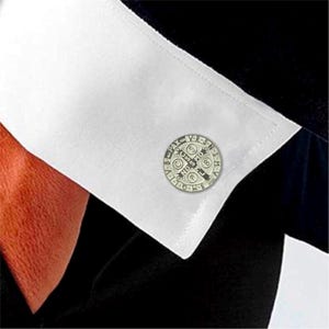 May include: Silver cufflinks with a circular design featuring a cross and the words "Pax" and "Vobis".