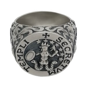 K&ouml;nnte beinhalten: Ein silberner Ring mit einem komplizierten Design, das eine Figur mit einem Schwert und einem Schild zeigt, umgeben von Sternen und dem Text "TEMPLI SECRETVM".