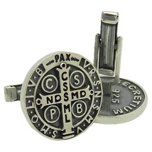 May include: Silver cufflinks with a black and silver Saint Benedict medal design. The medal features the inscription "Pax" and "V.R.S.N.S.M.V" around the edge. The back of the cufflinks are marked "925" and "ECRETIVM".