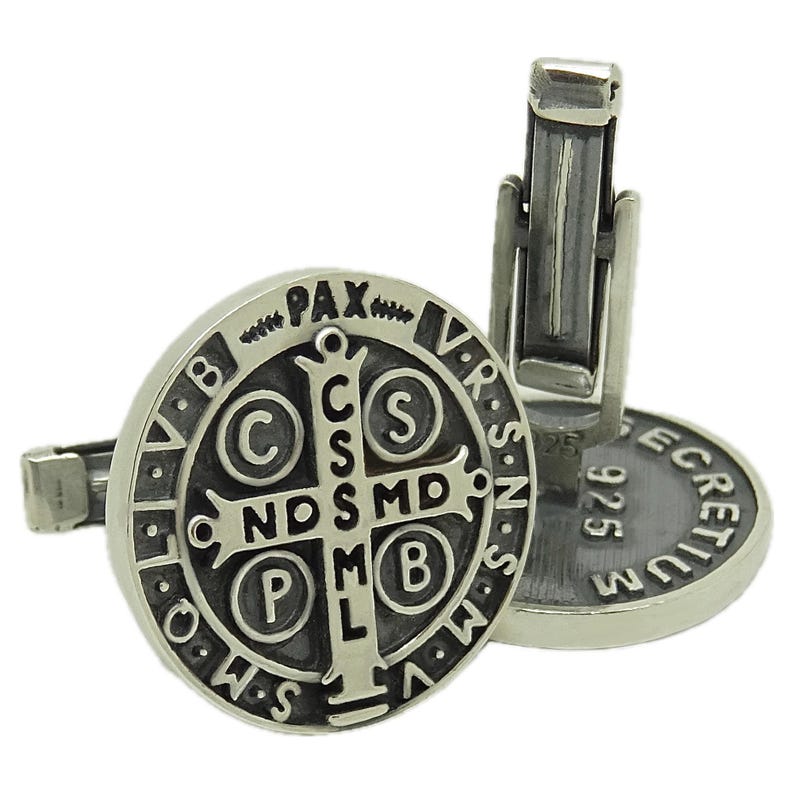May include: Silver cufflinks with a black and silver Saint Benedict medal design. The medal features the inscription "Pax" and "V.R.S.N.S.M.V" around the edge. The back of the cufflinks are marked "925" and "ECRETIVM".
