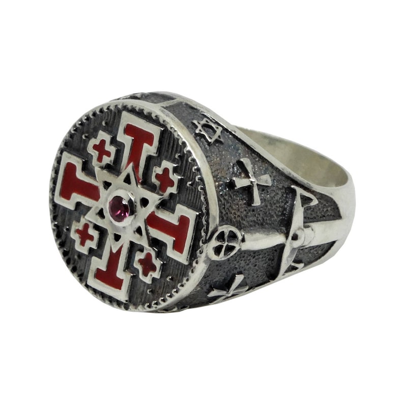 May include: A silver ring with a red and black enamel design featuring a cross and a star. The ring has a red gemstone in the center.