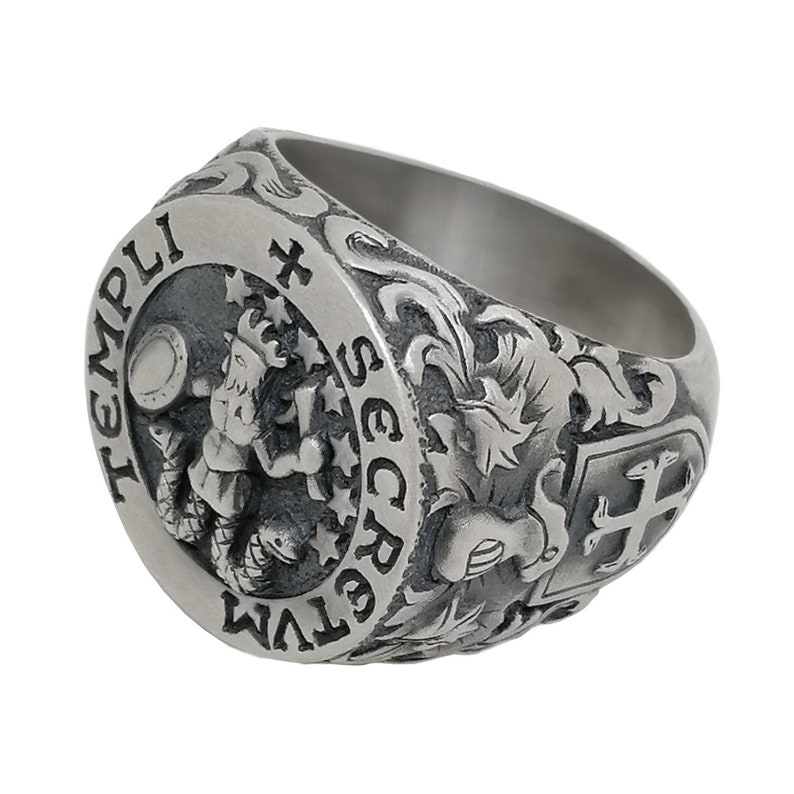 K&ouml;nnte beinhalten: Ein silberner Ring mit aufwendigen Gravuren. Der Ring zeigt ein Wappen mit einem Kreuz und einem Fabelwesen, umgeben von floralen Designs. Die Inschrift "TEMPLI SECRETVM" ist auf dem Ring zu sehen.