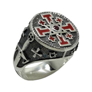 May include: A silver ring with a red enamel cross and a star of David design. The ring is detailed with other religious symbols.