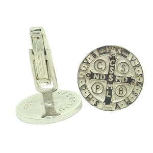 May include: Silver cufflinks featuring a Saint Benedict medal with a black cross and inscription. The back of the cufflinks are engraved with "925" and "SECRETIC".