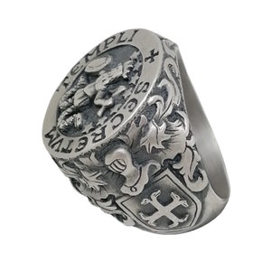 K&ouml;nnte beinhalten: Ein silberner Ring mit einem komplizierten Design, das ein Wappen mit einem Kreuz, einer gefl&uuml;gelten Kreatur und den Worten "CRETVM TEMPLI" zeigt.