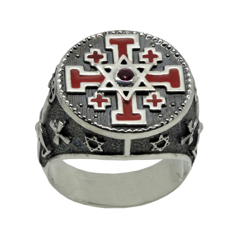 May include: A silver ring with a red enamel cross and a star of David in the center. The ring is decorated with small crosses and stars around the edge.