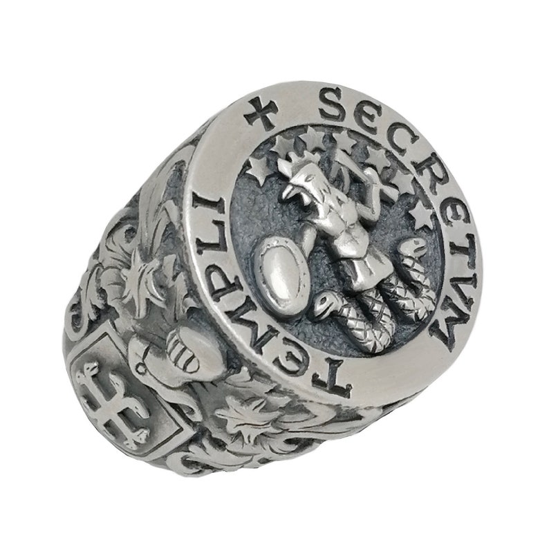 K&ouml;nnte beinhalten: Ein silberner Ring mit einem komplizierten Design, das eine gefl&uuml;gelte Figur zeigt, die einen Schild und eine Schlange h&auml;lt. Der Ring ist mit den Worten "Secretum Templi" und einem Kreuz beschriftet.