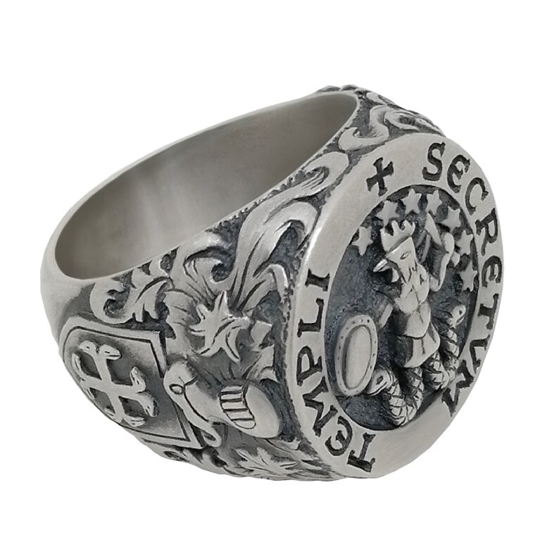 K&ouml;nnte beinhalten: Ein silberner Ring mit einem komplizierten Design, das ein Wappen mit einem Kreuz, einem Stern und einem Hut zeigt. Der Ring hat auch ein rundes Emblem mit einer Figur, die einen Schild und eine Schlange h&auml;lt, umgeben von Sternen und dem Text "TEMPLI SECRETUM".