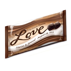 May include: A brown chocolate bar wrapper with the word "Love" in a cursive font. The wrapper also says "Silky Smooth Promises" and "Marion & Samuel August 28, 1955".